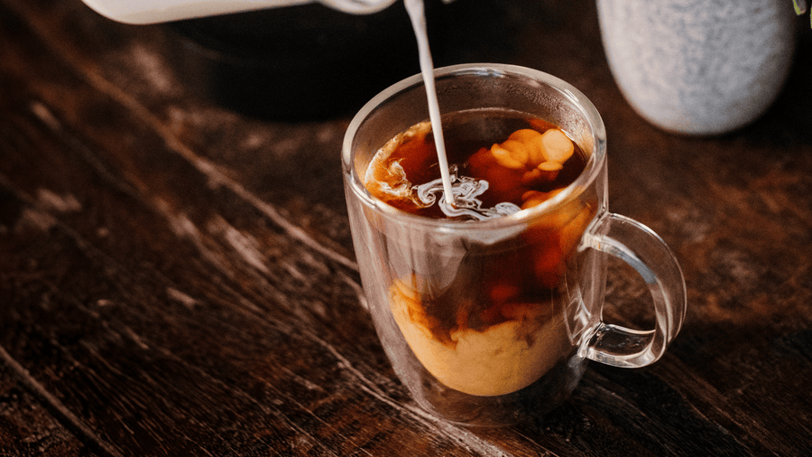 A cup of coffee with creamer being poured into it