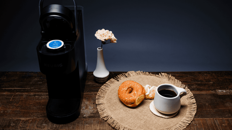 A cup of coffee and a donut next to a Keurig coffee maker