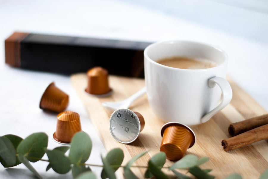 a coffee mug with coffee, coffee pods thrown around it