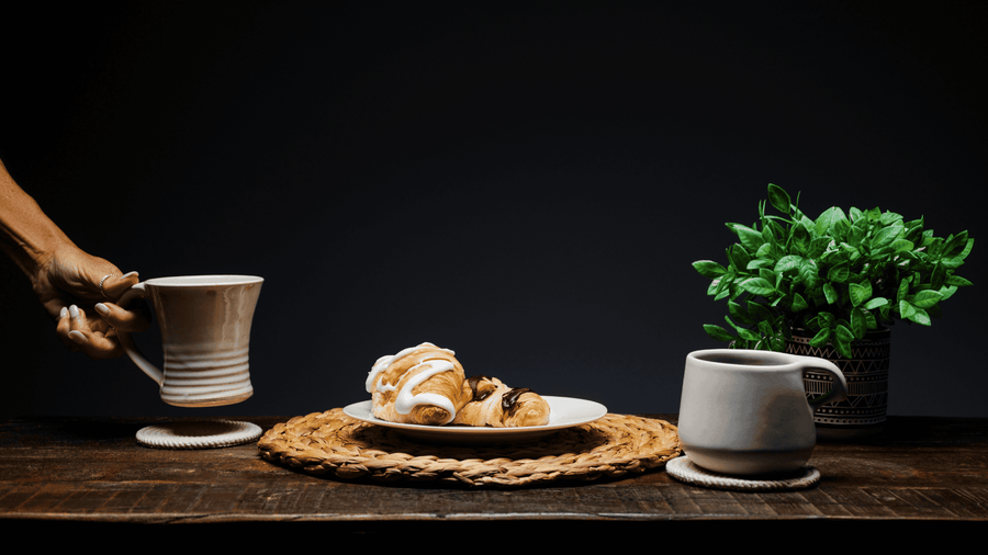 A person setting a coffee cup down on a plate next to some pastries