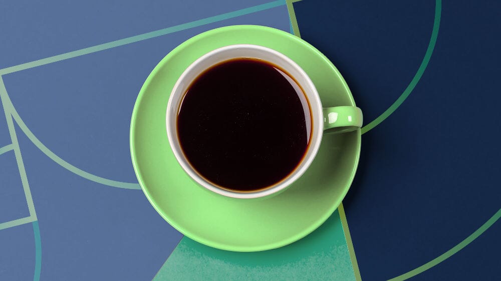 Green cup and saucer with black coffee on a blue geometric background