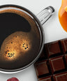 Cup of coffee with chocolate bars, caramel, and coffee beans on a white background